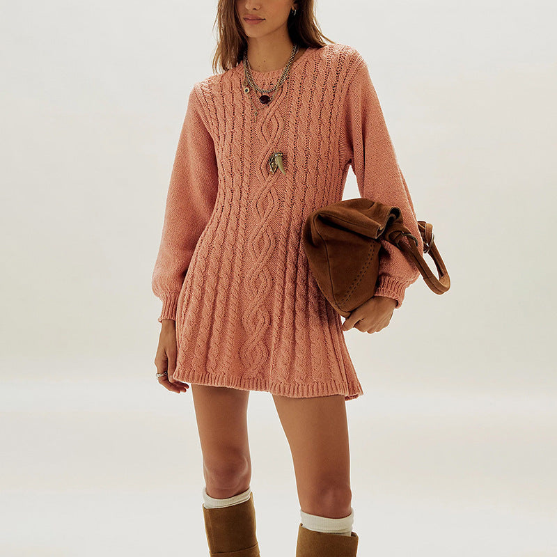 Woman in an orange cable knit dress with ribbed cuffs and a long necklace, holding a brown bag, front view