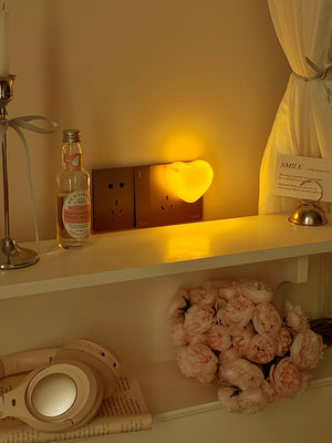 Warm amber heart night light glowing beside a wall socket in a cozy room