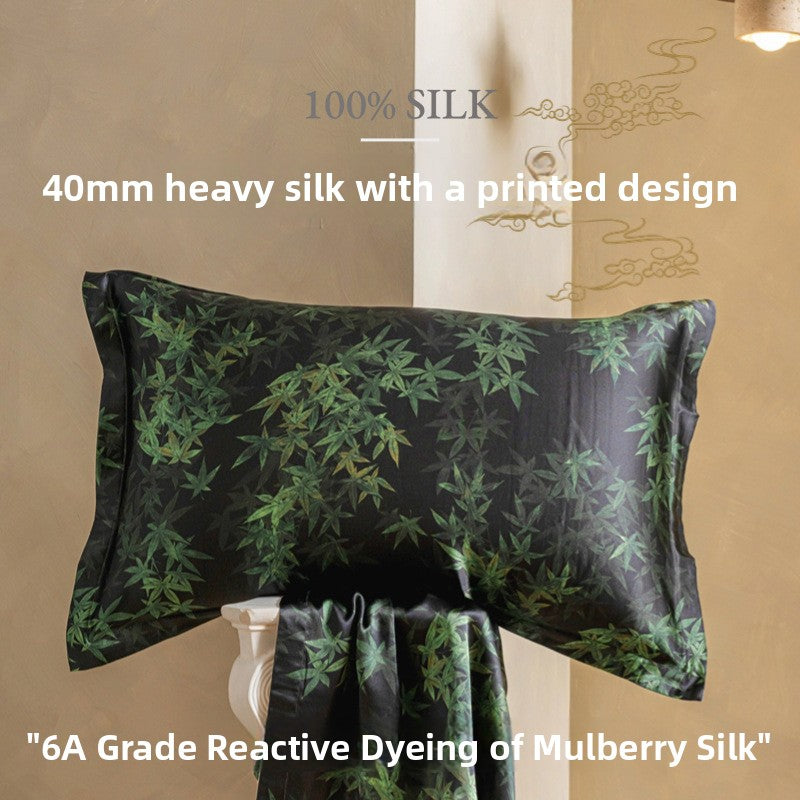 Dark charcoal silk pillowcase printed with green leaves, with matching printed silk fabric draped below it