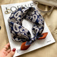 Navy paisley printed square scarf with a satin sheen and hemmed edges, shown displayed and knotted