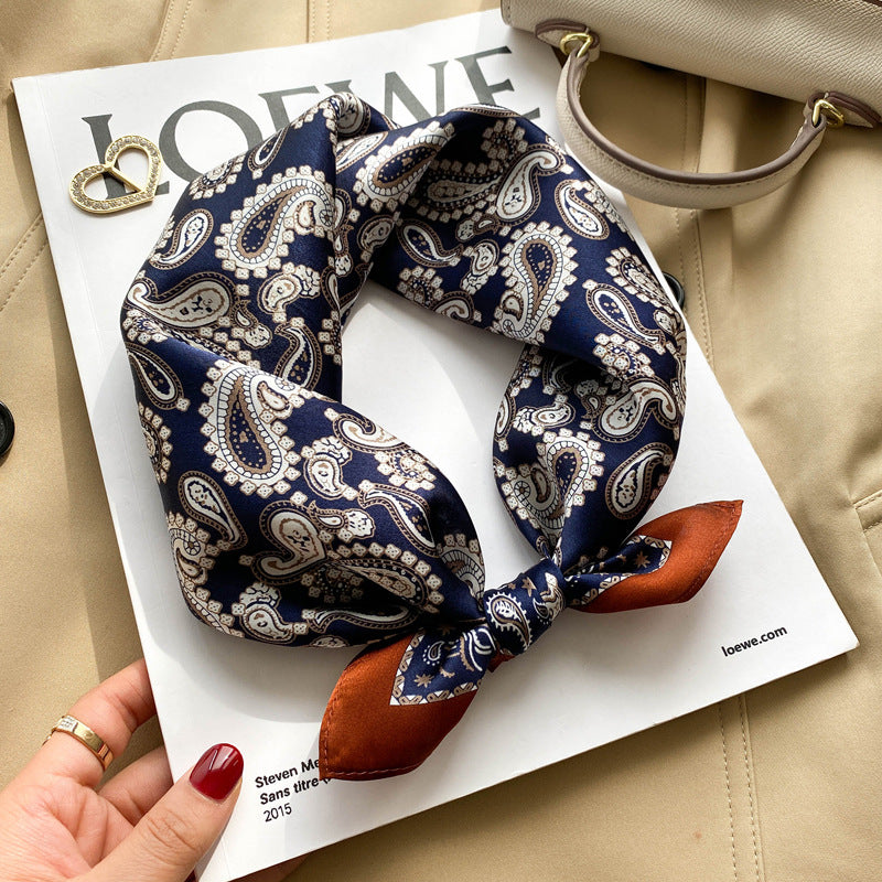 Navy paisley printed square scarf with a satin sheen and hemmed edges, shown displayed and knotted