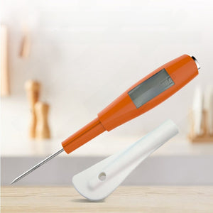 Orange handled digital food thermometer with a steel probe and white silicone scraper in a kitchen