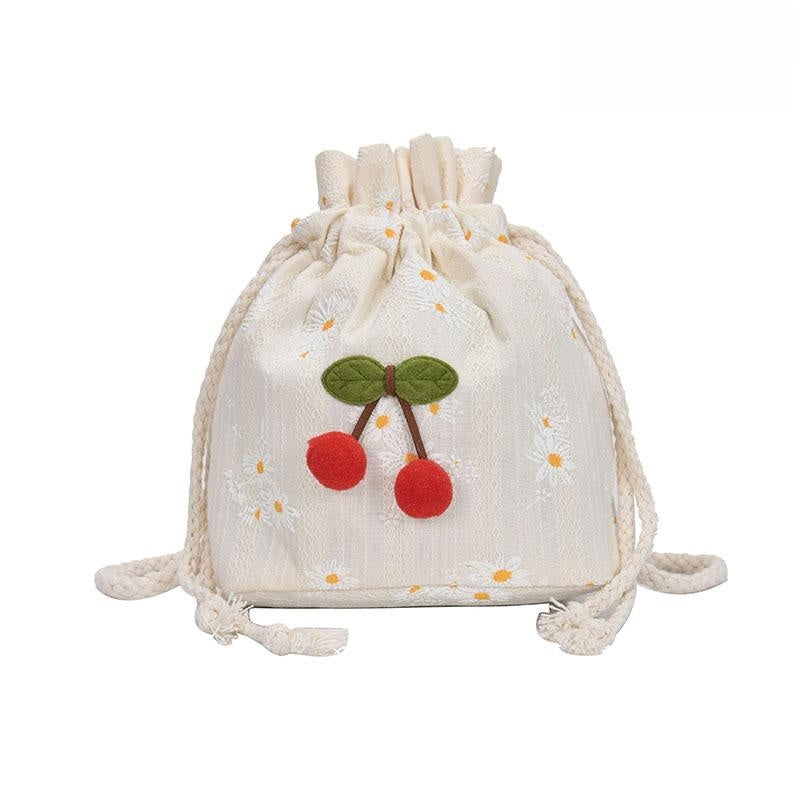 Front view of small daisy embroidered canvas bucket bag with red cherry charm detail