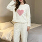 Cream plush fleece pajama top with a pink plush heart patch and wide leg pants, front view in a bedroom