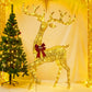 Large golden lit reindeer with a red bow stepping beside a decorated Christmas tree in a warm yellow room
