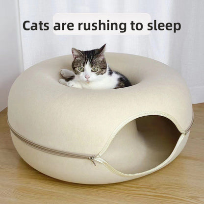 Beige felt donut cat bed with a tabby cat curled in the hollow centre on a wooden floor