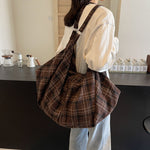 Woman carrying a large slouchy brown woolen plaid shoulder tote bag with an adjustable strap