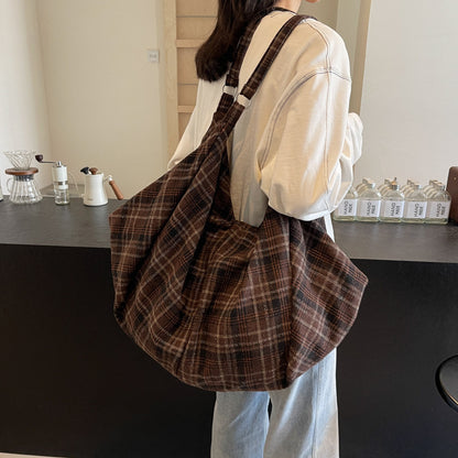 Woman carrying a large slouchy brown woolen plaid shoulder tote bag with an adjustable strap
