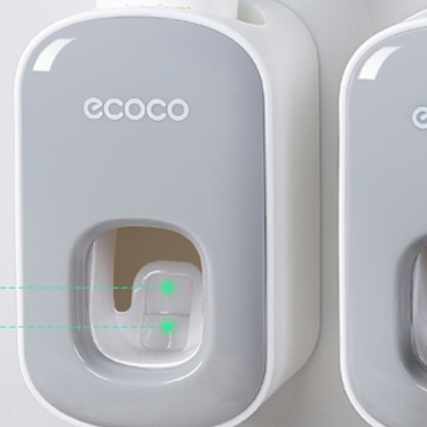 Close view of a grey toothpaste dispenser front showing the soft pad window where paste comes out