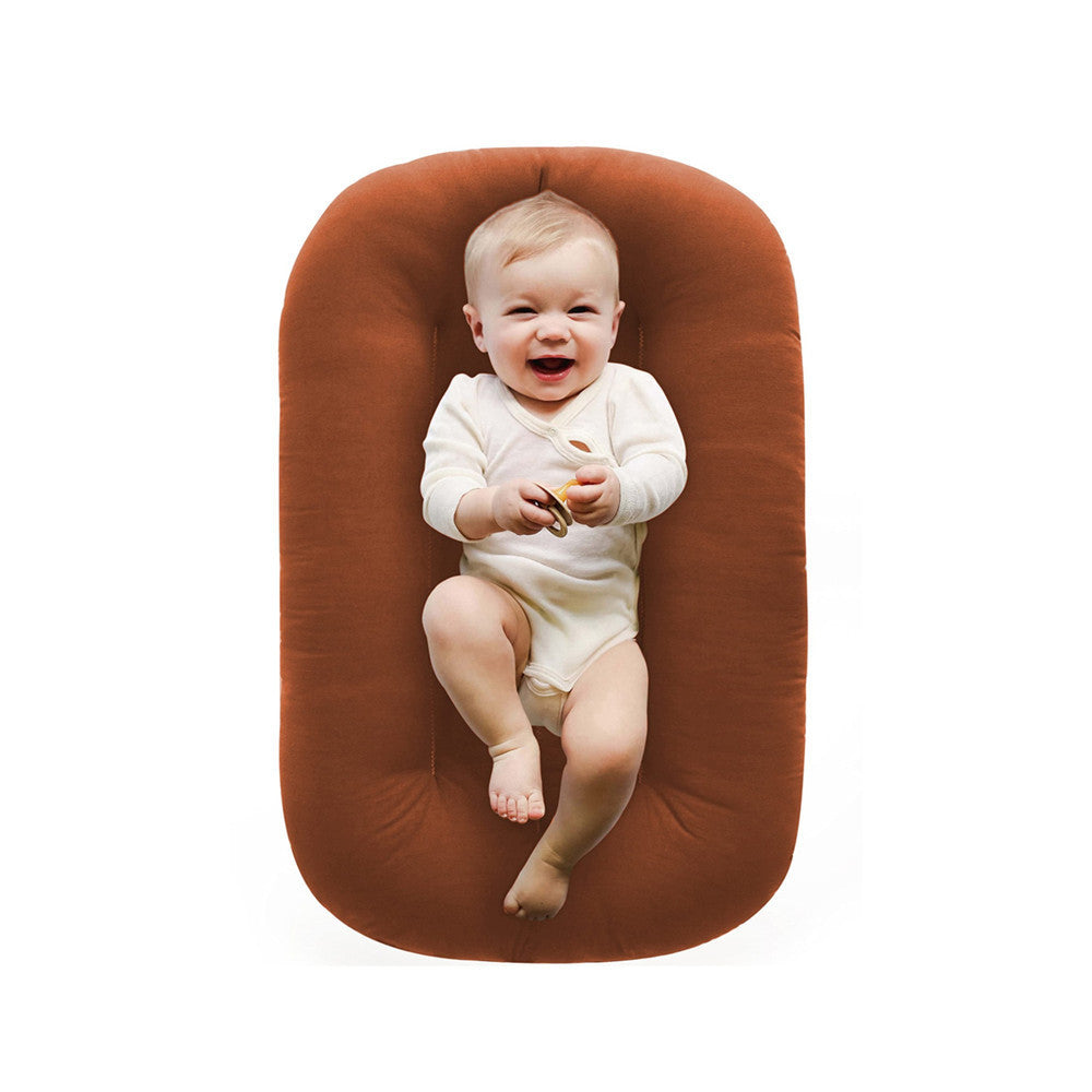 Baby lounger nest set beside an adult on a soft surface for supervised cuddles