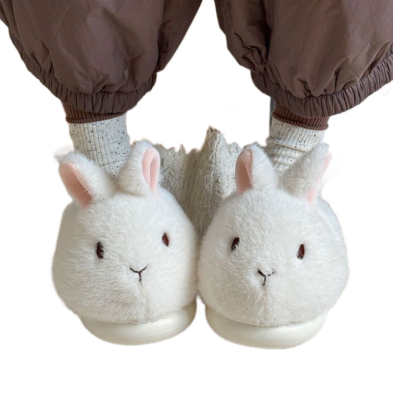 White bunny plush slippers worn with brown gathered trousers and gray socks on a plain white background