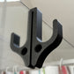 Black resin double hook with two round holes over the top edge of a glass shower door, textured finish