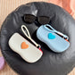 Gray white and blue silicone sunglasses cases with raised hearts and wrist lanyards near sunglasses