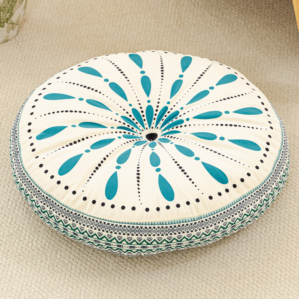 Round cushion with a teal teardrop sunburst and black dots on a cream top with a teal woven border