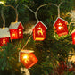 Red wooden house string lights with reindeer cut-outs glowing among Christmas tree branches