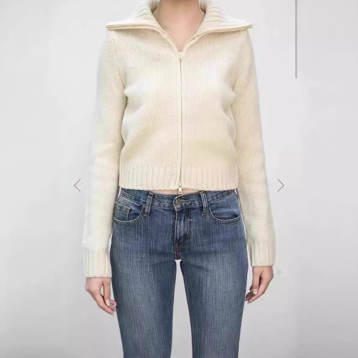 Woman wearing cream knit zip cardigan with wide ribbed collar and ribbed hem over blue jeans, front view