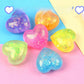 Six glitter heart squeeze toys grouped on pastel paper, gold sequins visible through the gel