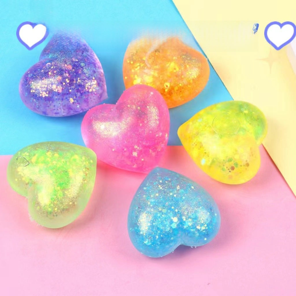 Six glitter heart squeeze toys grouped on pastel paper, gold sequins visible through the gel