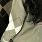 Matcha green sweater with a cream diamond sleeve seen from behind, black and tan argyle sweater of another colourway at left