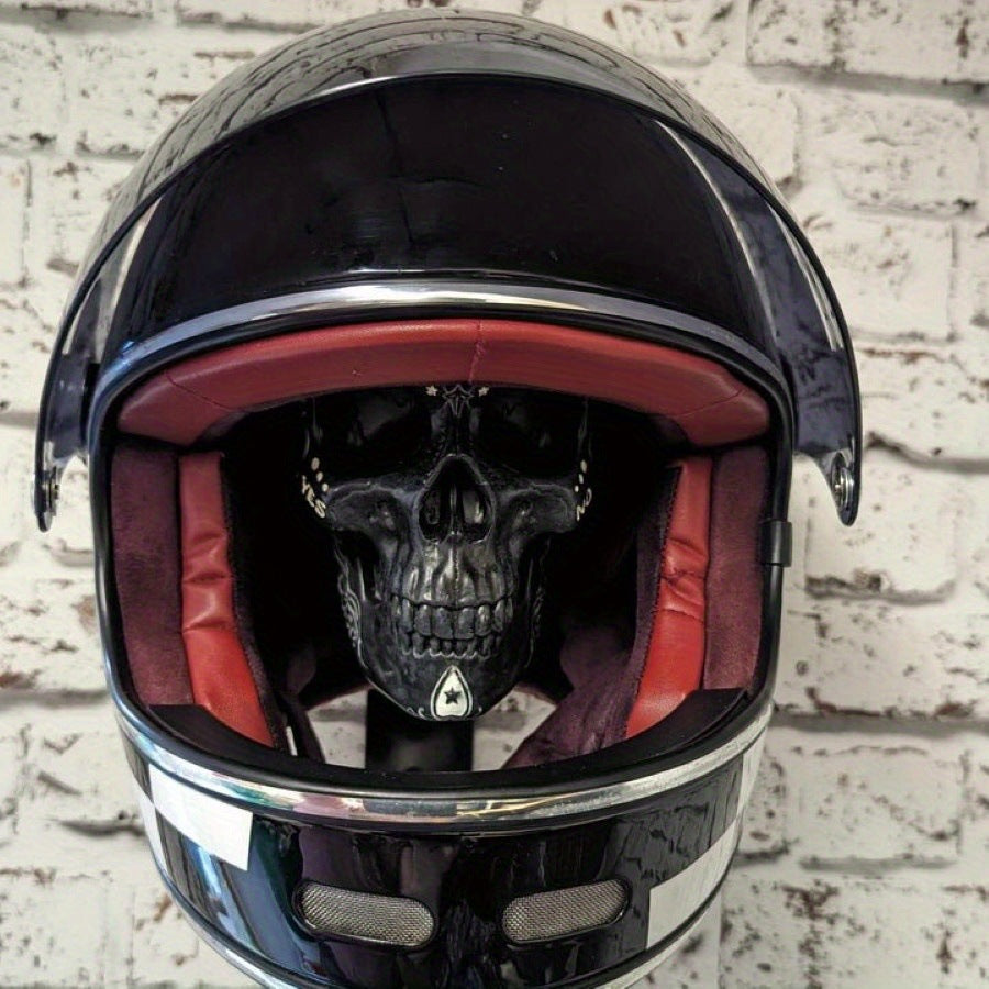 Black resin skull helmet rack holding a black full face motorcycle helmet on a brick wall