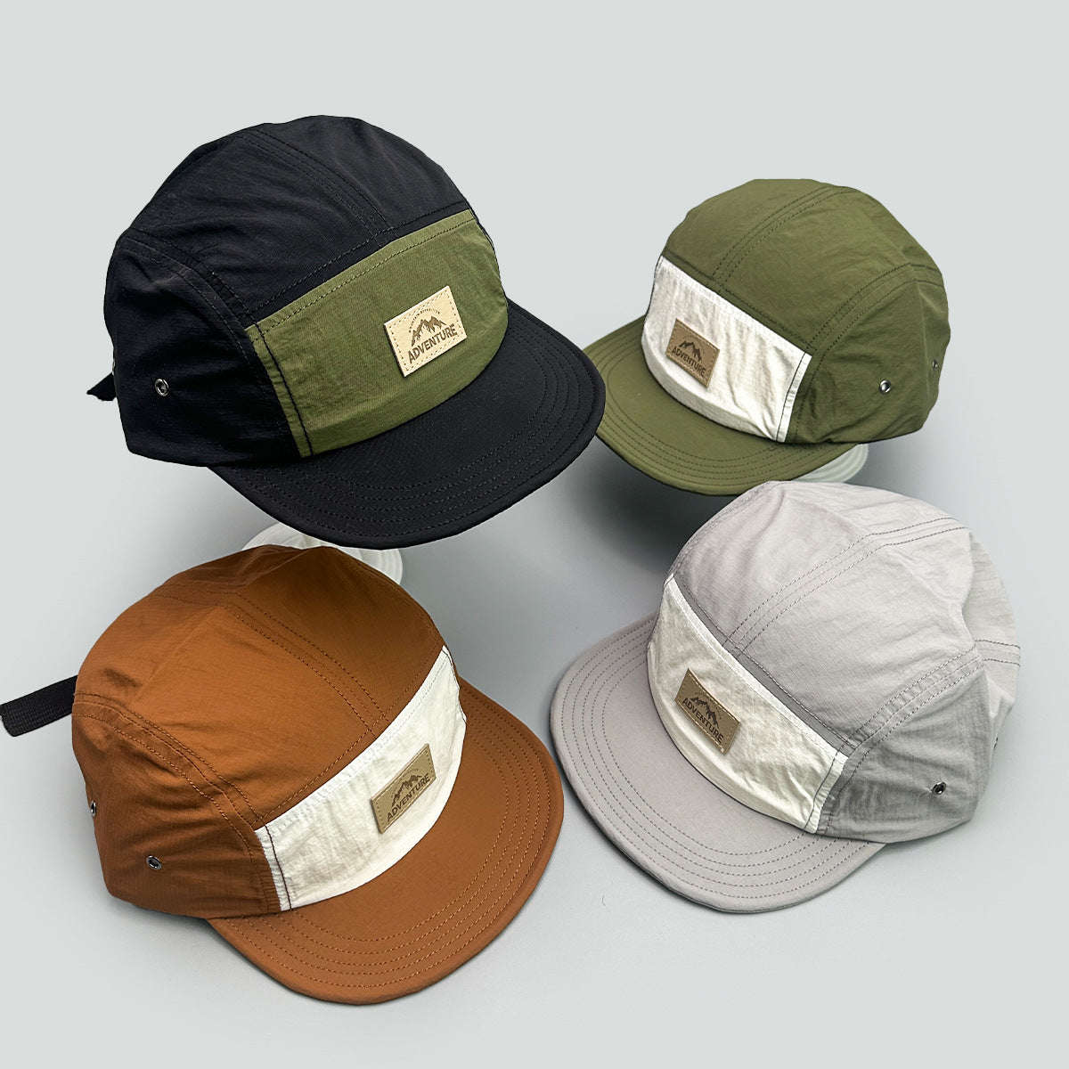Four flat brim camp caps in black green, olive, camel and grey laid out to show the contrast front panels