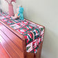 Christmas table runner with Santa and stocking pattern in green and red squares on a sideboard, 33x45 cm option