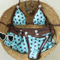 Polka dot bikini set flat on a straw hat, triangle top above the tie side brief with white buttons