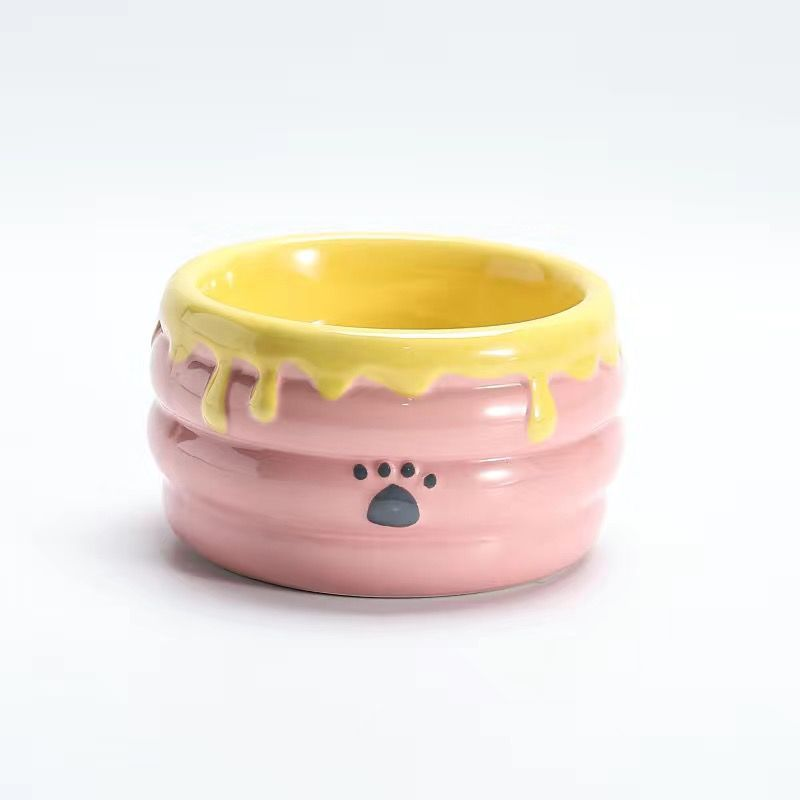 Pink ceramic honey jar bowl with a yellow dripping glaze rim and a paw print on a white background