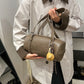 Woman holding a gray brown cylinder shoulder bag by its long straps with a baseball glove charm