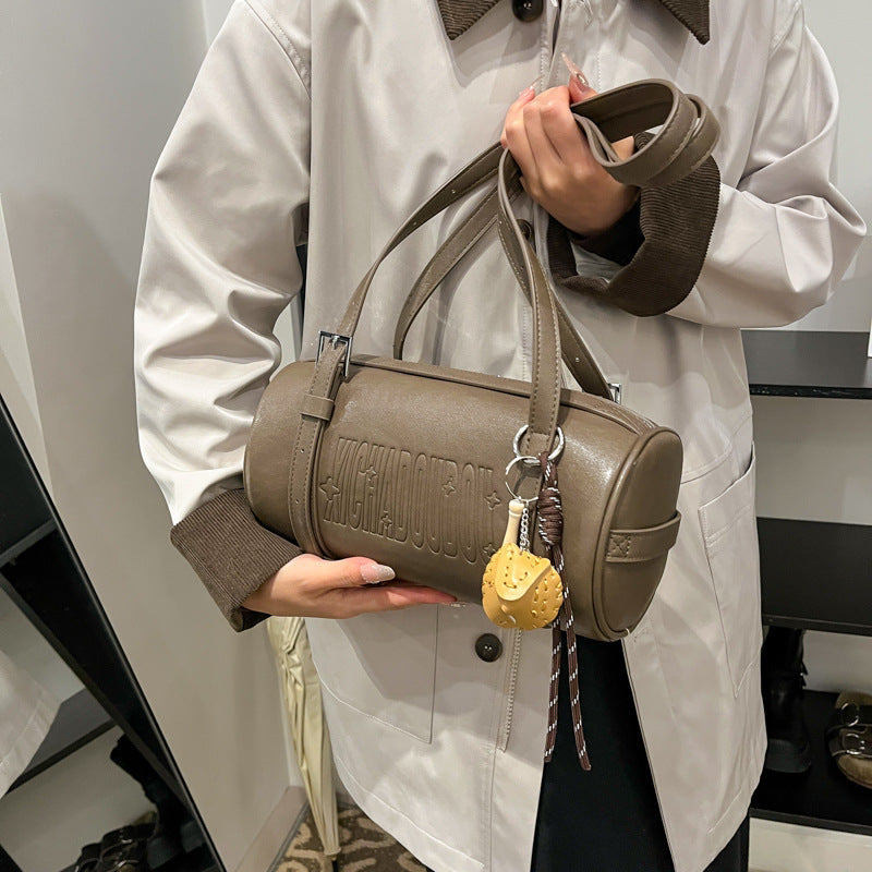 Woman holding a gray brown cylinder shoulder bag by its long straps with a baseball glove charm