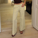 Beige wide leg trousers with a deep folded cuff, front view on a model standing on a wooden floor
