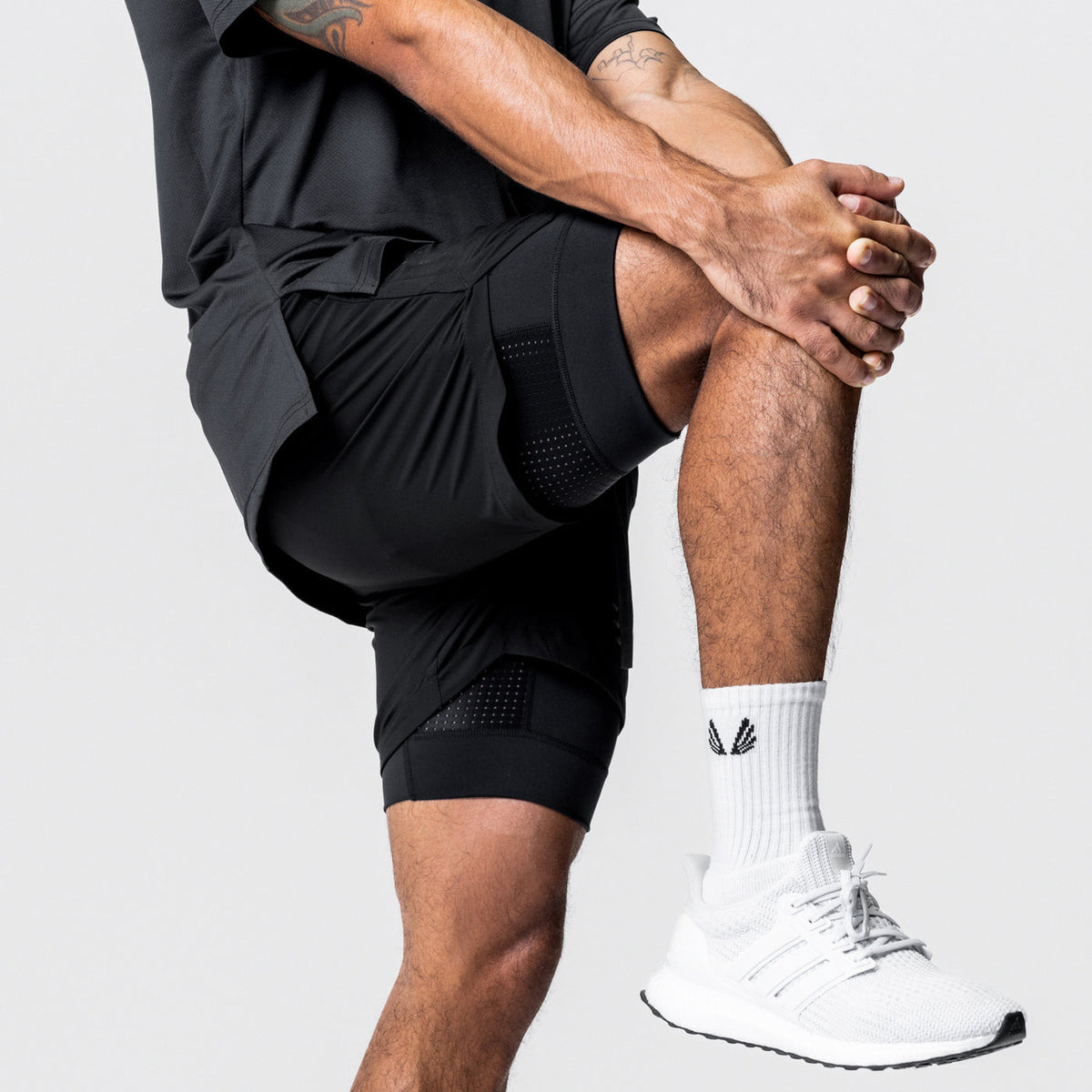 Man wearing the two in one training shorts in black, stretching, showing the fitted inner liner