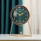 Emerald green dial pendulum desk clock with black bezel, gold hands and a triangular gold tone stand on a white table
