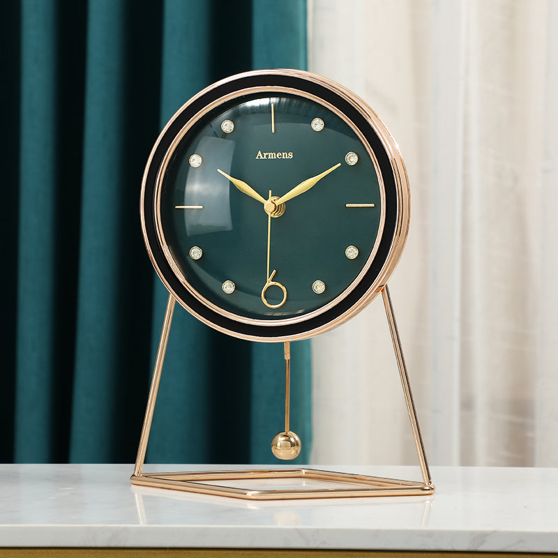 Emerald green dial pendulum desk clock with black bezel, gold hands and a triangular gold tone stand on a white table