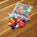 Sheer white drawstring pouch spilling assorted PVC middle finger novelty figures onto a wooden table