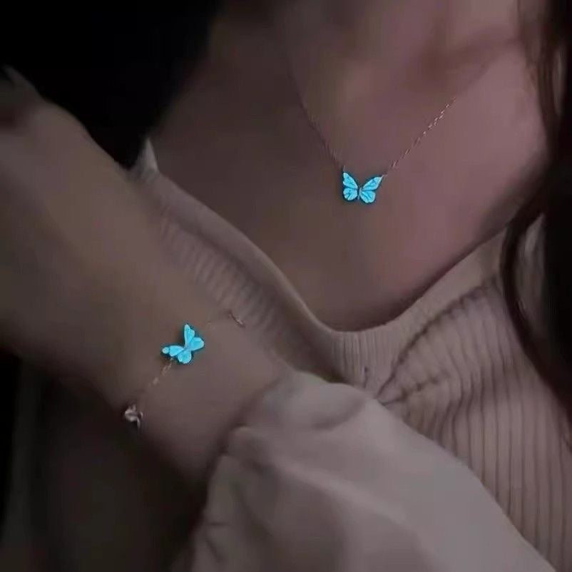 Glowing blue butterfly pendant held up on a fine silver tone chain necklace