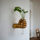 Gold metallic fist wall vase holding a glass tube with a leafy cutting
