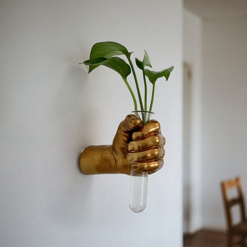 Gold metallic fist wall vase holding a glass tube with a leafy cutting