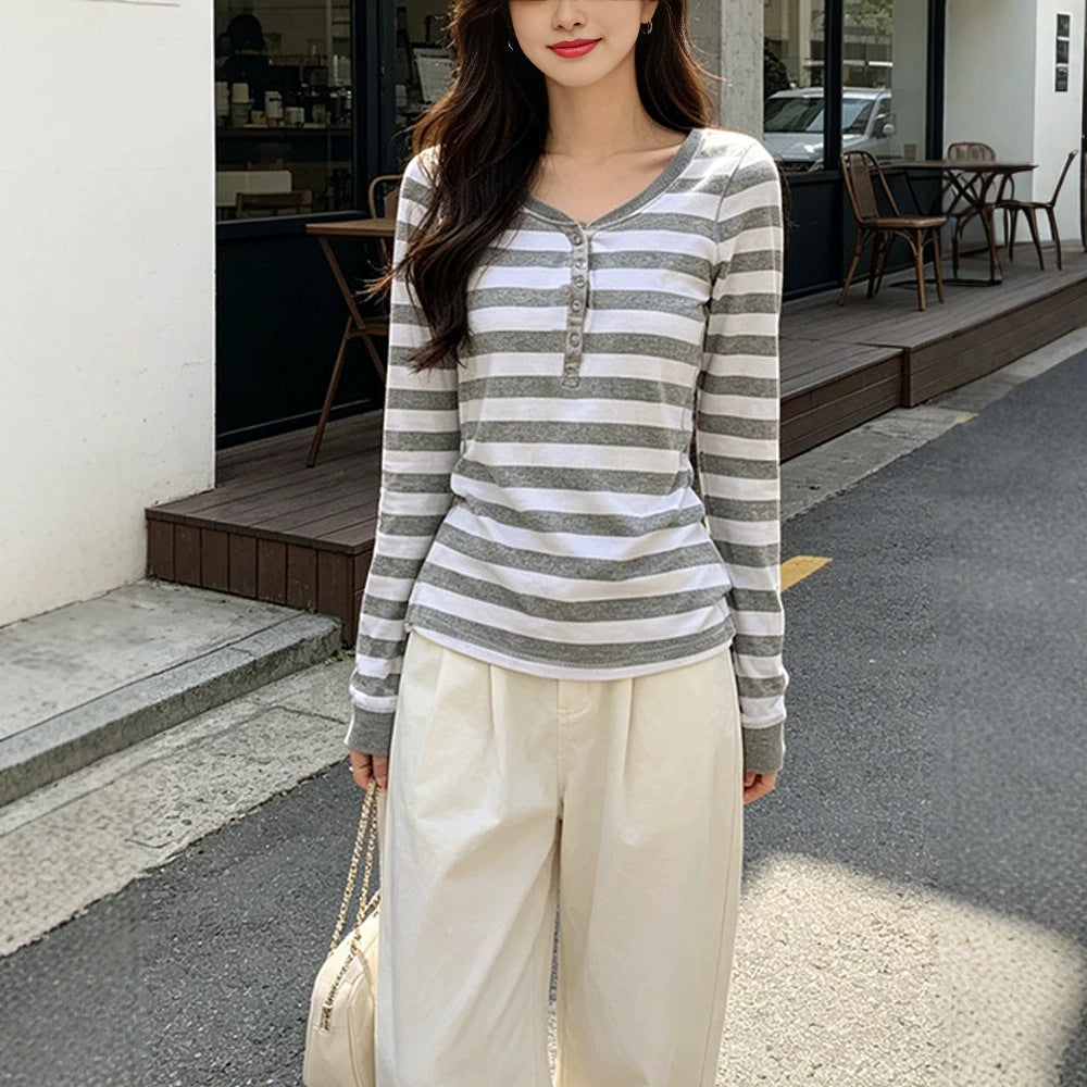 Woman wearing a gray and white striped henley top with cream wide leg trousers on a city street, front view