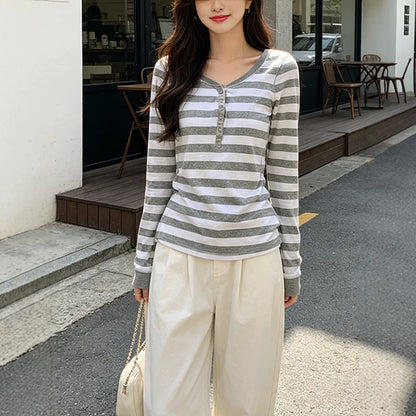 Woman wearing a gray and white striped henley top with cream wide leg trousers on a city street, front view