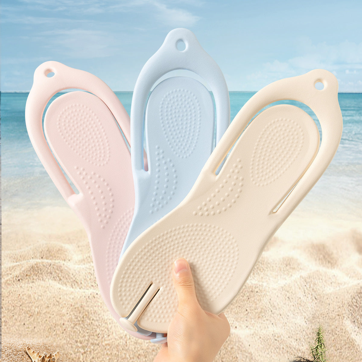 Three folded EVA travel flip flops in pink, blue and cream held up in one hand at the beach