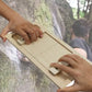 Two hands pulling the wooden grip bars of the trainer board against a rock face background
