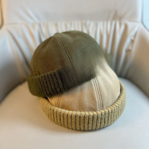 Army green and khaki brimless caps with ribbed knit cuffs stacked on a pale armchair