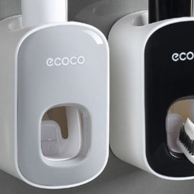 Grey and black wall mounted toothpaste dispensers side by side showing the front dispensing window