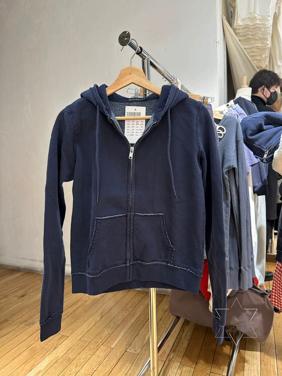 Navy zip-up hoodie with drawstring hood and raw edge seams on a clothes rack, with a size label inside the hood