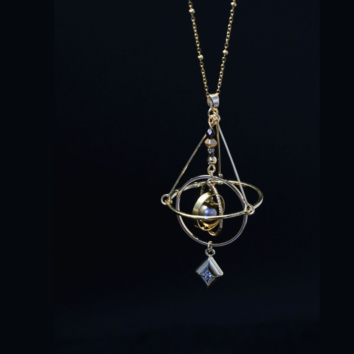 Gold tone armillary sphere pendant with kite charm and blue stone hanging below the rings