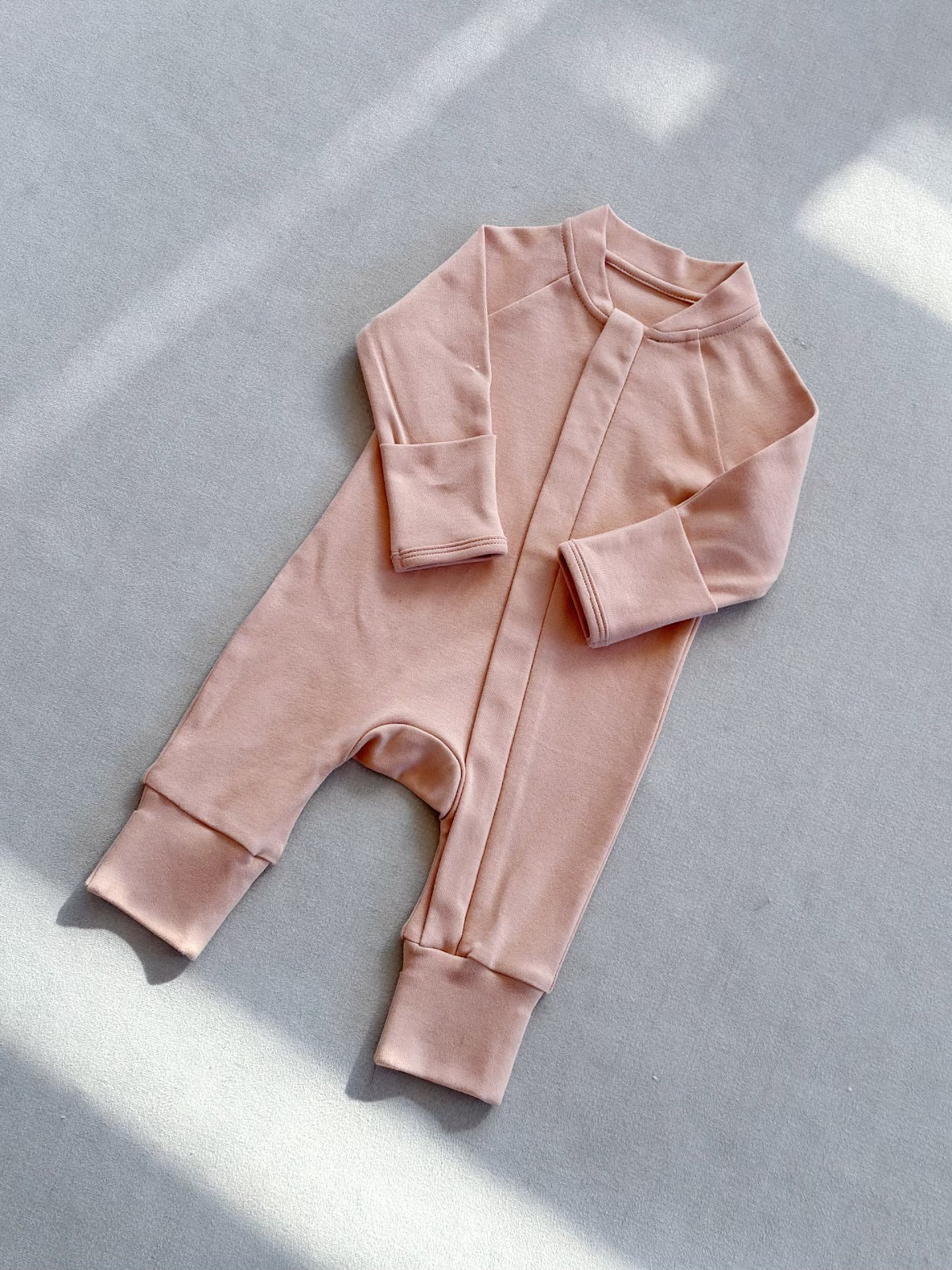Baby Pink zip front baby romper laid flat on a gray floor, image of the 66 cm, 3 to 6 months size option