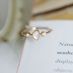 Dainty gold-tone ring with teardrop white cabochon and two opal accents on an open book