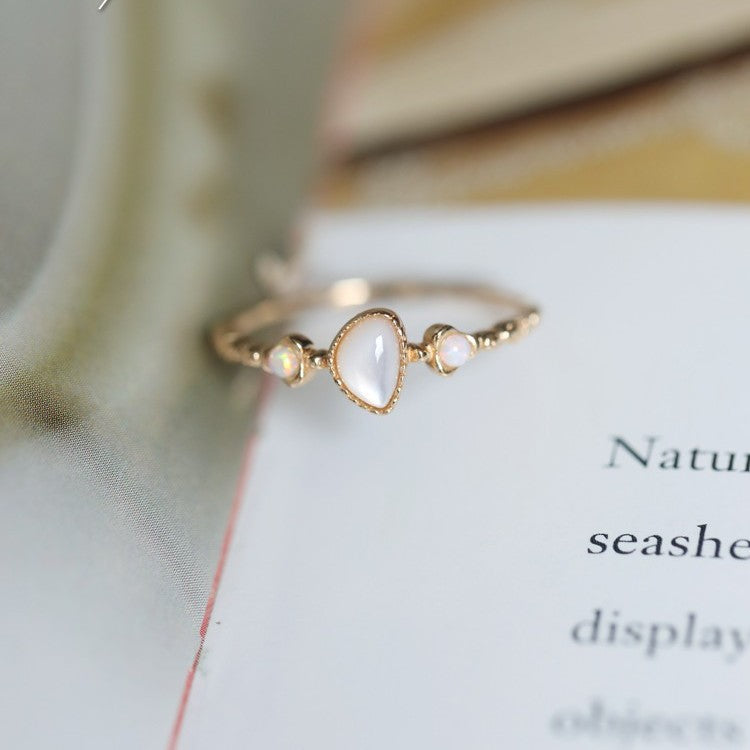 Dainty gold-tone ring with teardrop white cabochon and two opal accents on an open book