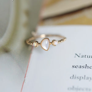 Dainty gold-tone ring with teardrop white cabochon and two opal accents on an open book